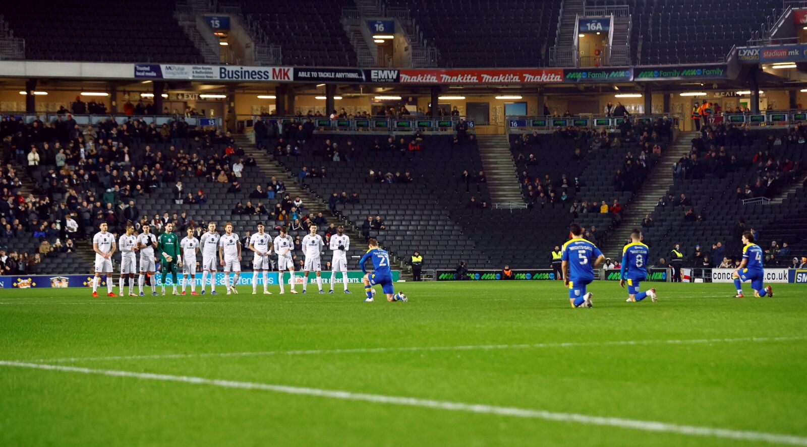 Soccer Football - League One - Milton Keynes Dons v AFC Wimbledon - Stadium MK, Milton Keynes, Britain - January 11, 2022 Milton Keynes Dons players stand together as AFC Wimbledon players kneel before the match Action Images/Andrew Boyers  EDITORIAL USE ONLY. No use with unauthorized audio, video, data, fixture lists, club/league logos or 